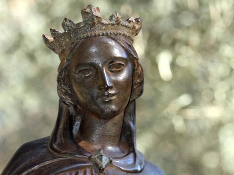 Bronzestatue einer jungen Frau mit Krone, die mild lächelt, in einem Park stehend.