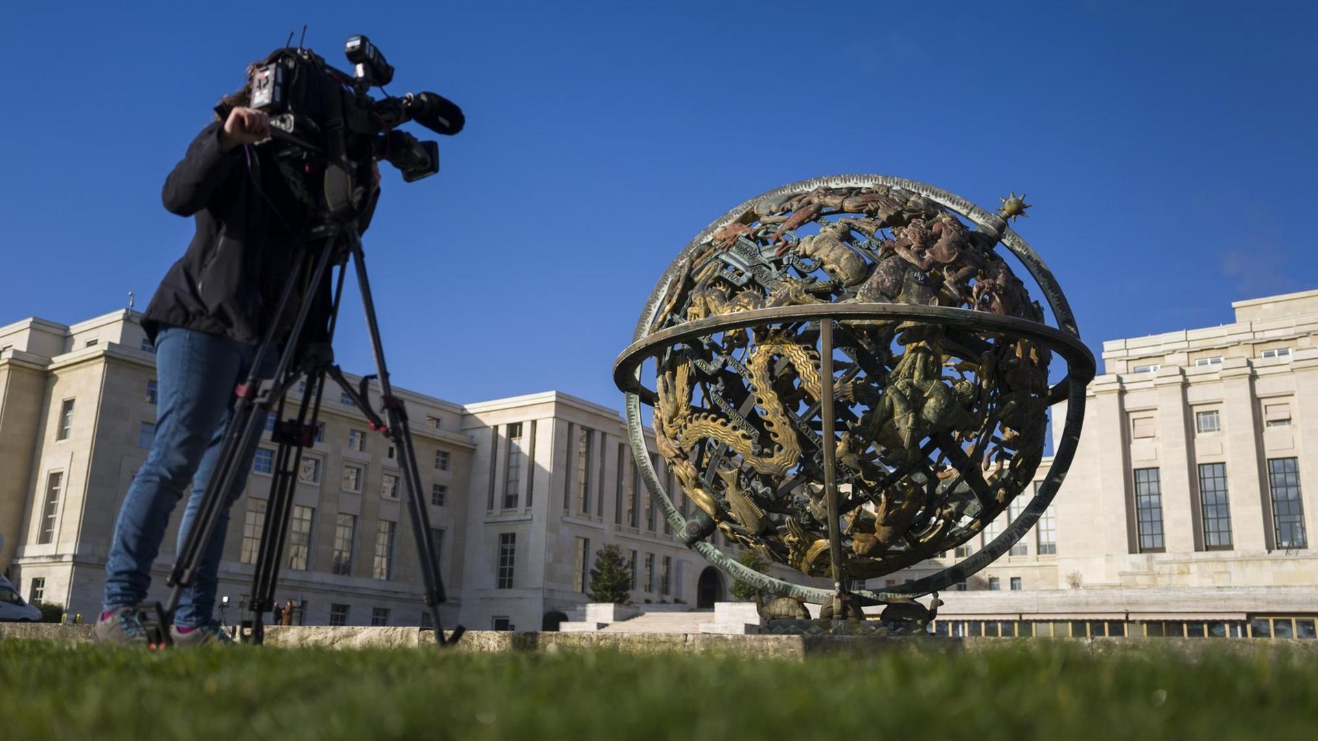 Im Hintergrund das Gebäude der UNO in Genf, davor eine Weltkugel-Skulptur und ein filmender Kameramann.