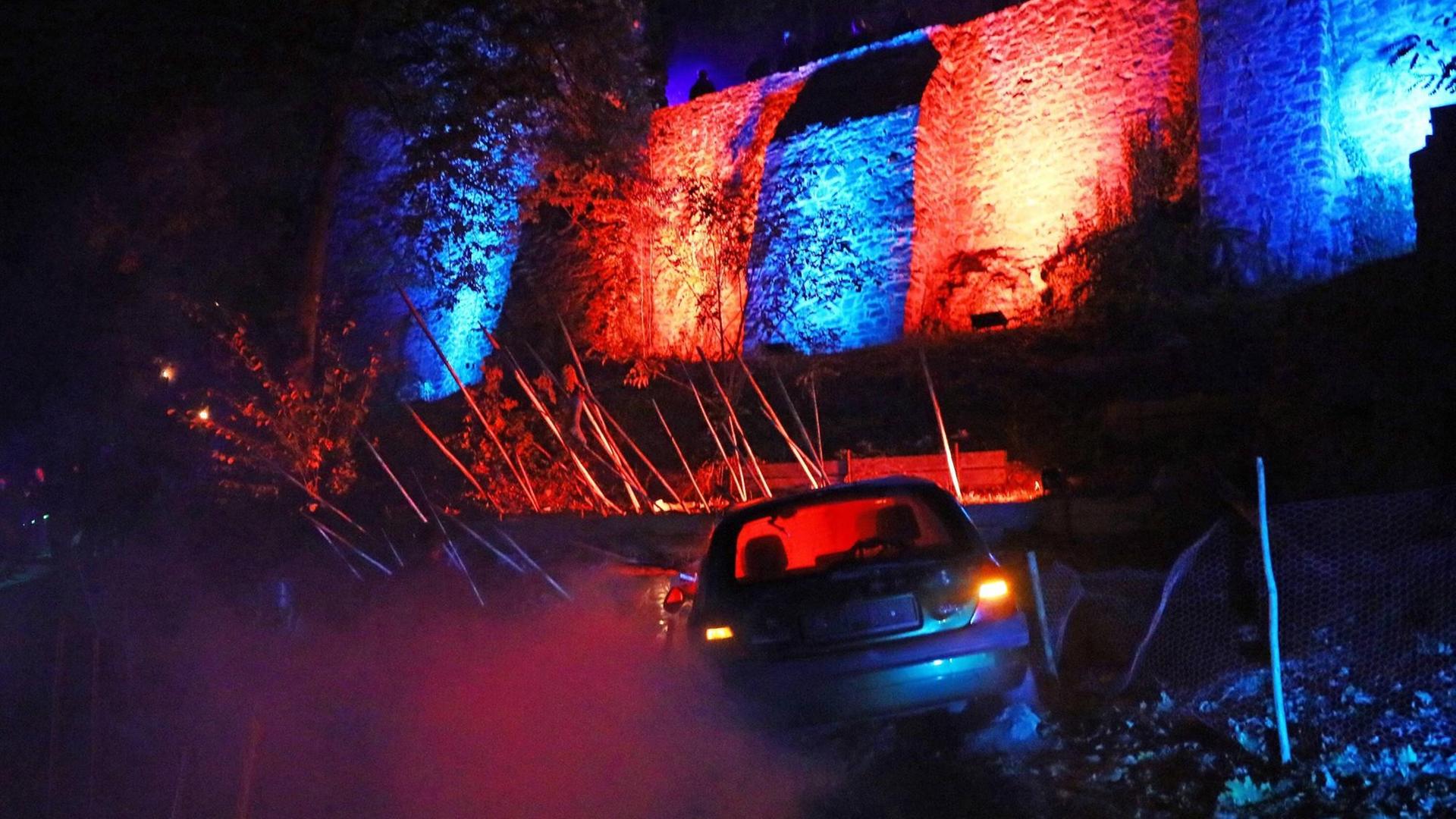 Vor einer rot-blau angestrahlten Mauer steht ein Auto. Eine Szene bei der Zombie-Apokalypse in Mühltal. Vor einer rot-blau angestrahlten Mauer steht ein Auto. Eine Szene bei der Zombie-Apokalypse in Mühltal.