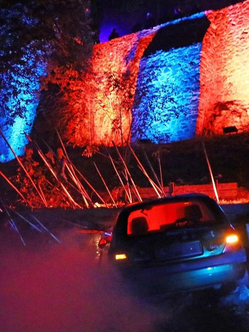 Vor einer rot-blau angestrahlten Mauer steht ein Auto. Eine Szene bei der Zombie-Apokalypse in Mühltal.