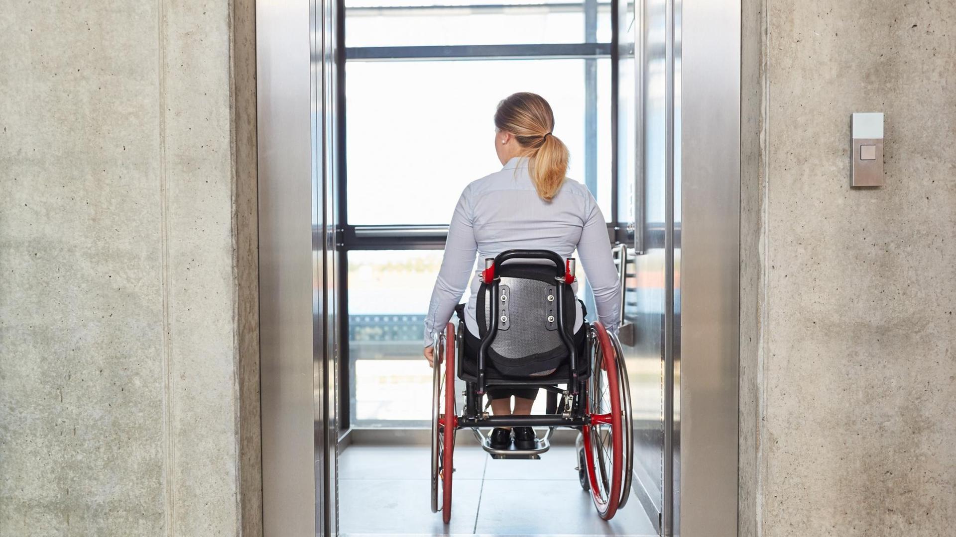 Eine Geschäftsfrau im Rollstuhl fährt mit dem Fahrstuhl in einem Geschäftsgebäude.