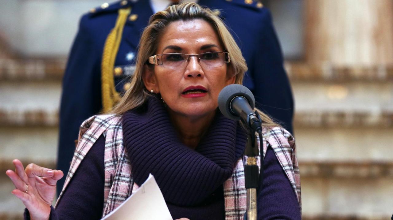 Die bolivianische Übergangspräsidentin Jeanine Áñez am 21. November im Palacio de Gobierno, dem bolivianischen Regierungssitz in La Paz. Eine Frau mit langen blonden Haaren und einer Brille sitzt vor einem Mikrofon und spricht. Die bolivianische Übergangspräsidentin Jeanine Áñez am 21. November im Palacio de Gobierno, dem bolivianischen Regierungssitz in La Paz. Eine Frau mit langen blonden Haaren und einer Brille sitzt vor einem Mikrofon und spricht.