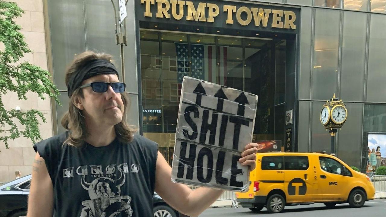 Ein Mann verkauft vor dem Trump Tower in New York Anti-Trump-Buttons und hält ein Schild hoch mit dem Slogan "Shit Hole"