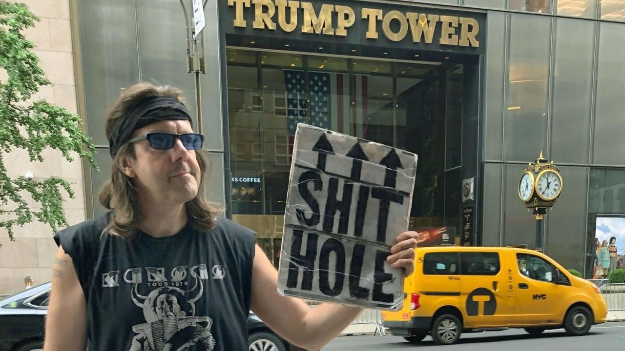 Ein Mann verkauft vor dem Trump Tower in New York Anti-Trump-Buttons und hält ein Schild hoch mit dem Slogan "Shit Hole" Ein Mann verkauft vor dem Trump Tower in New York Anti-Trump-Buttons und hält ein Schild hoch mit dem Slogan "Shit Hole"