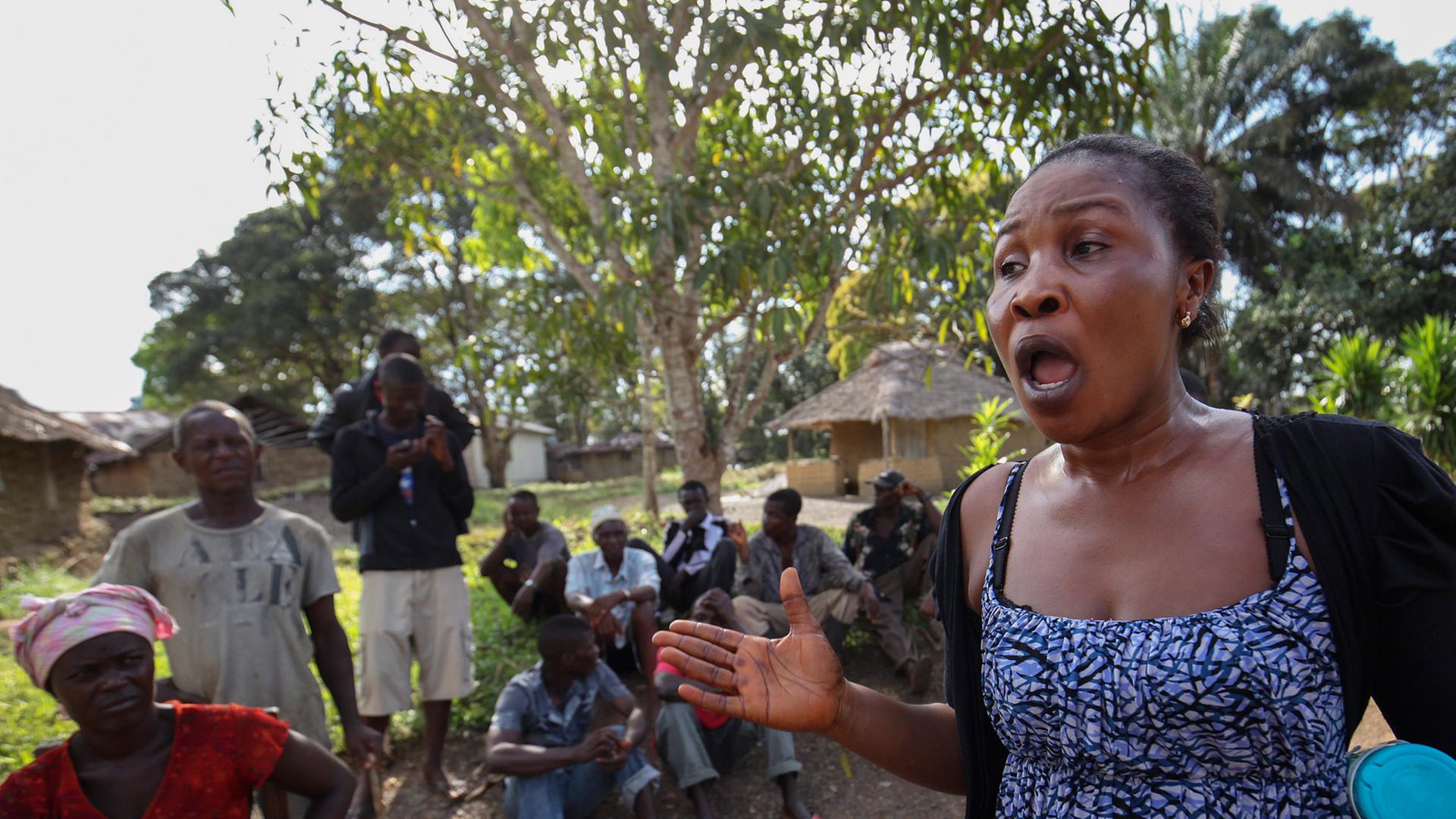 Eine klagende Frau in einem Dorf in Liberia, hinter ihr sitzen ein Dutzend Menschen Eine klagende Frau in einem Dorf in Liberia, hinter ihr sitzen ein Dutzend Menschen