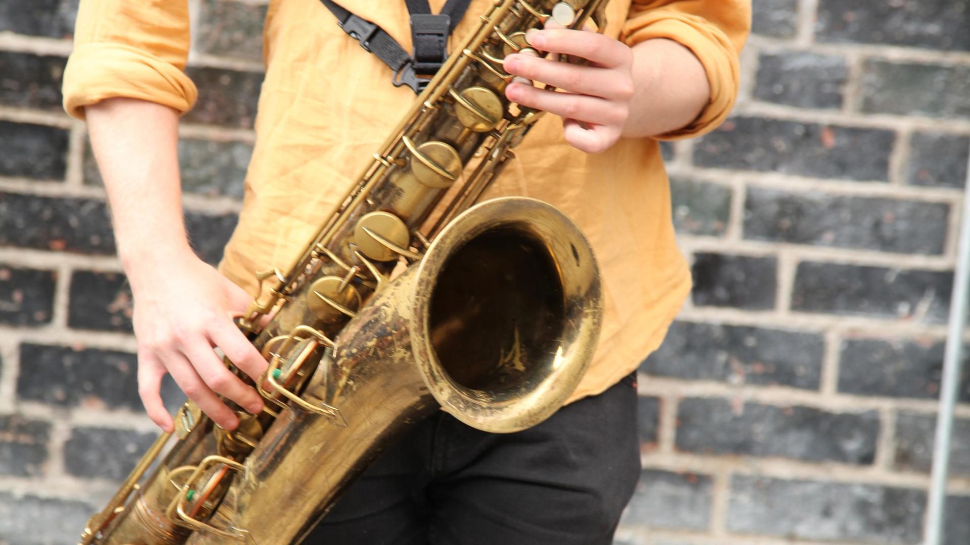 Ein junger Mann spielt in einer Fußgängerzone auf einem Saxofon. Ein junger Mann spielt in einer Fußgängerzone auf einem Saxofon.