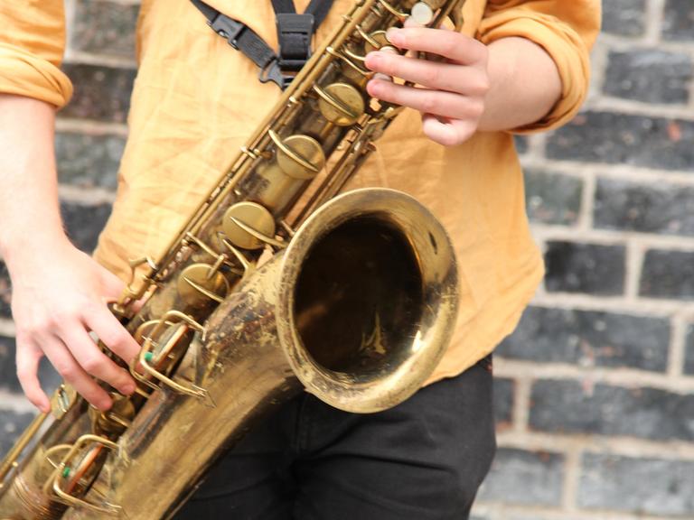 Ein junger Mann spielt in einer Fußgängerzone auf einem Saxofon.