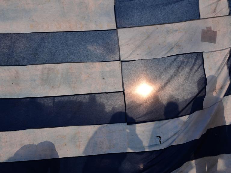 Demonstranten hinter einer griechischen Flagge in Athen