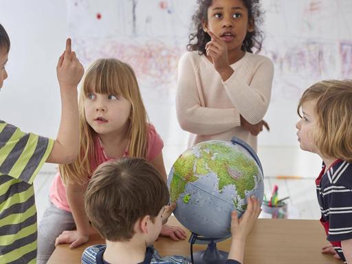 Diskutierende Kinder um einen Tisch, mit einem Globus.