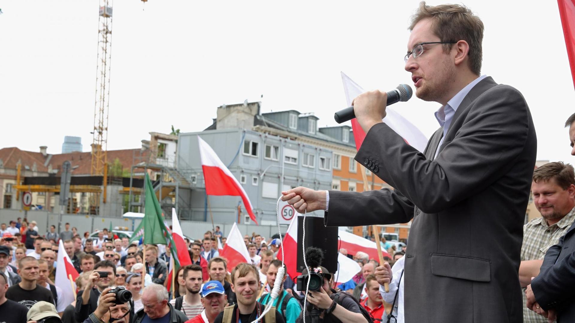 Robert Winnicki von der polnischen, rechtskonservativen "Nationalen Bewegung" spricht auf einer Demo zu einer Menschenmasse, er hält ein zu einem Galgen geknotetes Seil in der Hand.