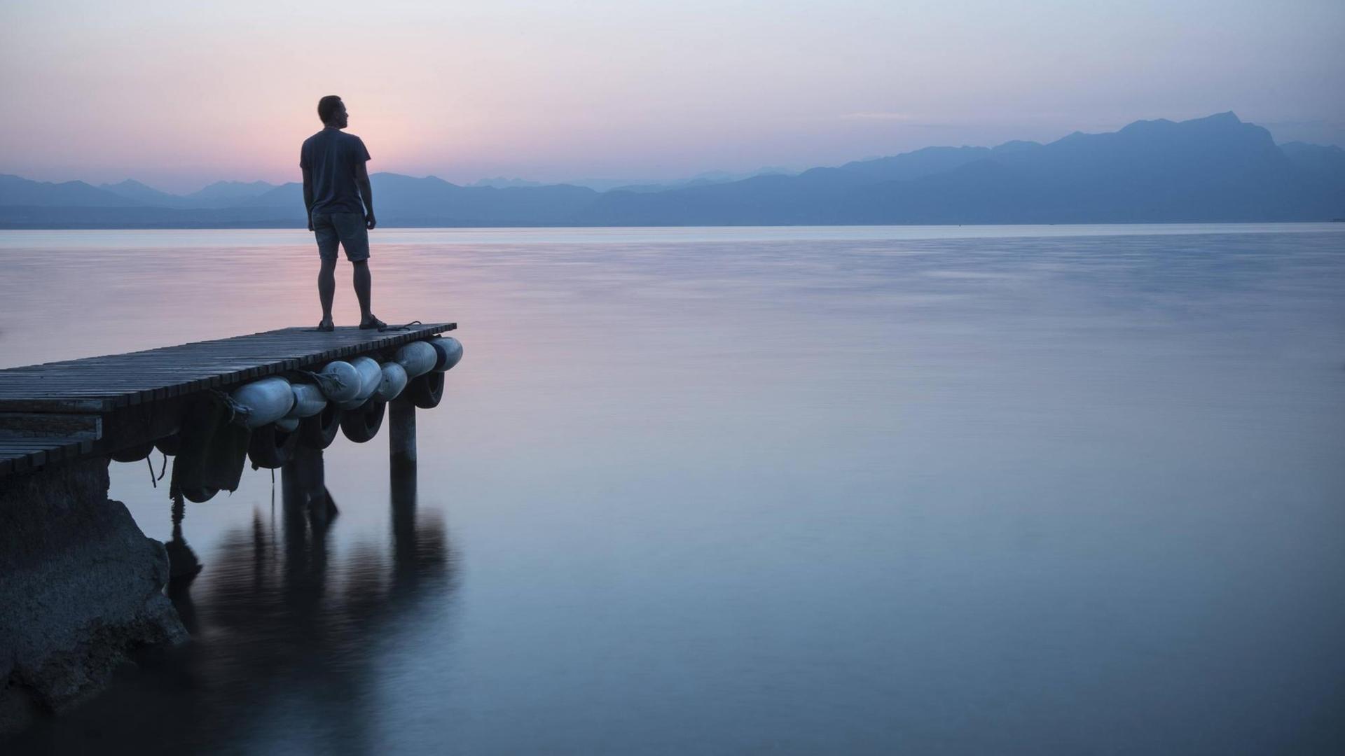 Ein Mann steht auf einem Steg am Gardasee in Italien, in Lazise. Ein Mann steht auf einem Steg am Gardasee in Italien, in Lazise.