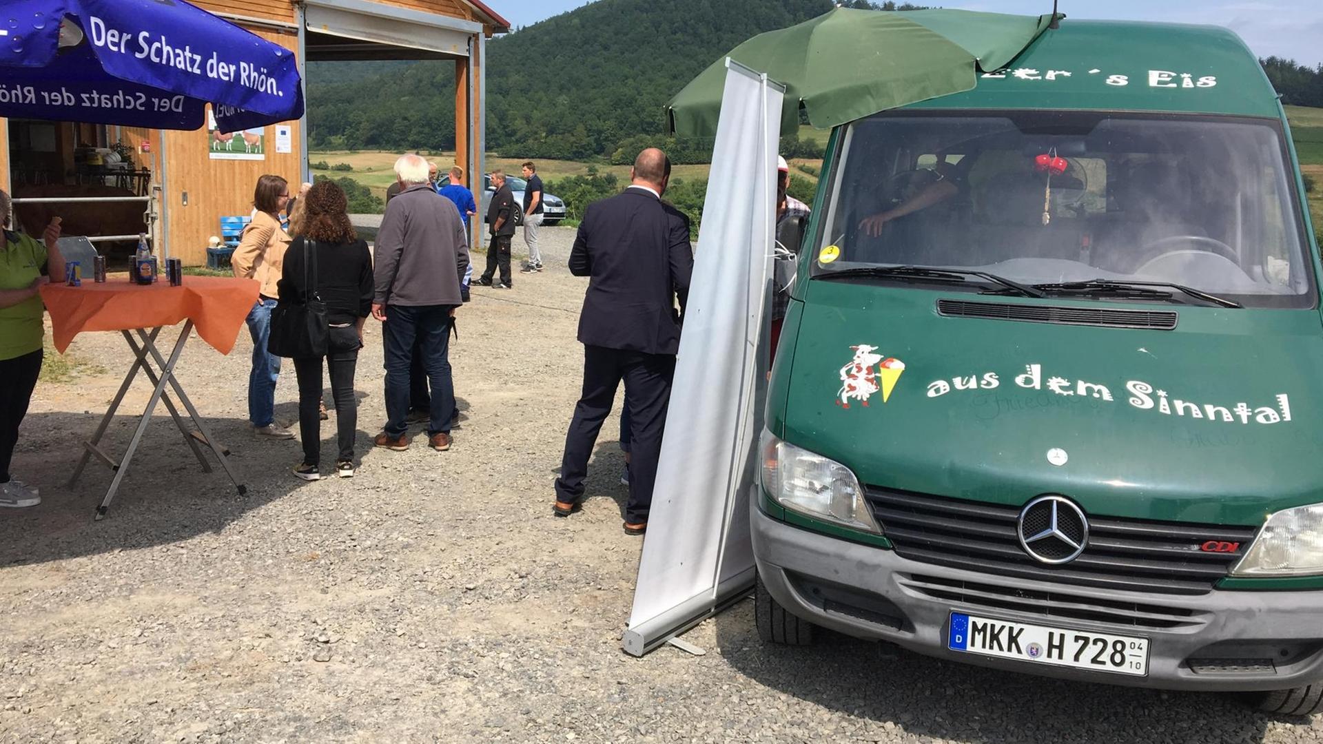 Ein Eiswagen steht vor einen Stallgebäude, mehrere Menschen stehen bei einem Hoffest am Wagen und unter einem Schirm. Ein Eiswagen steht vor einen Stallgebäude, mehrere Menschen stehen bei einem Hoffest am Wagen und unter einem Schirm.