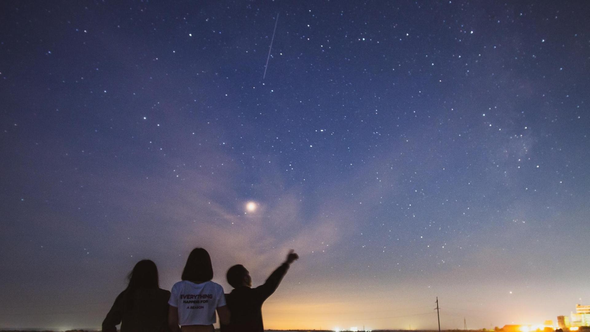 Drei Sillhouetten vor dem Abendhimmel mit Sternen und einer Sternschnuppe