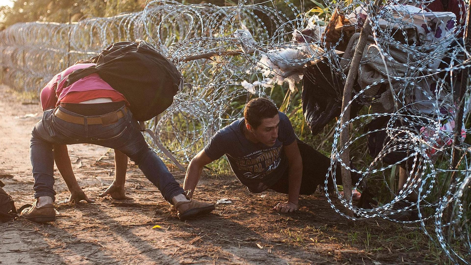Migranten drängen sich durch einen Stachdeldrahtzaun. Migranten drängen sich durch einen Stachdeldrahtzaun.
