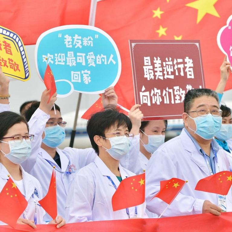 Krankenhausmitarbeiter in der chinesischen Stadt Nanning, mit Kittel und Mundschutz bekleidet, halten Schilder und chinesische Flaggen hoch.