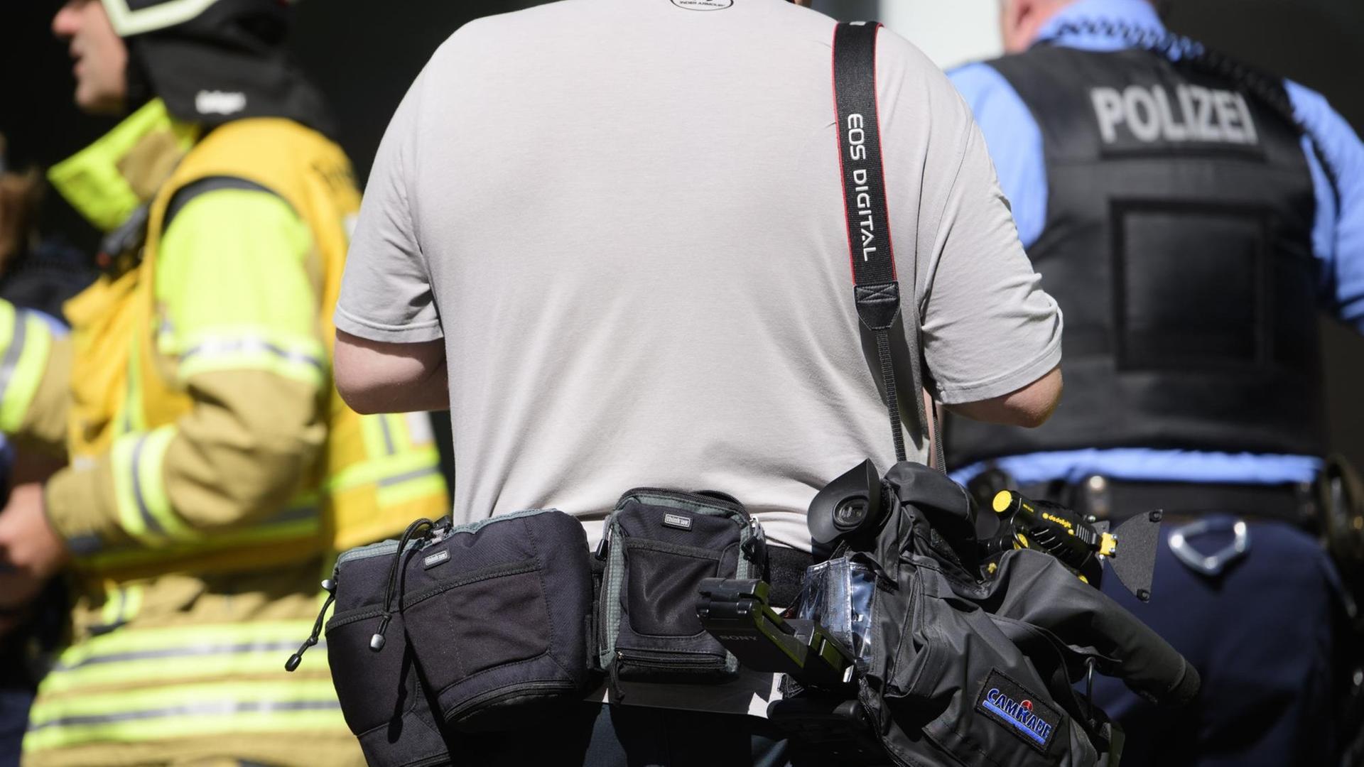 Ein sogenannter Blaulichtreporter steht während eines Feuerwehreinsatzes hinter einem Feuerwehrmann und einem Polizisten. Ein sogenannter Blaulichtreporter steht während eines Feuerwehreinsatzes hinter einem Feuerwehrmann und einem Polizisten.