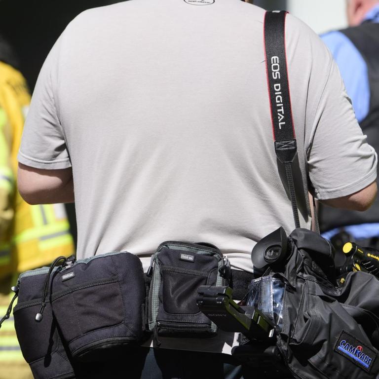 Ein sogenannter Blaulichtreporter steht während eines Feuerwehreinsatzes hinter einem Feuerwehrmann und einem Polizisten.