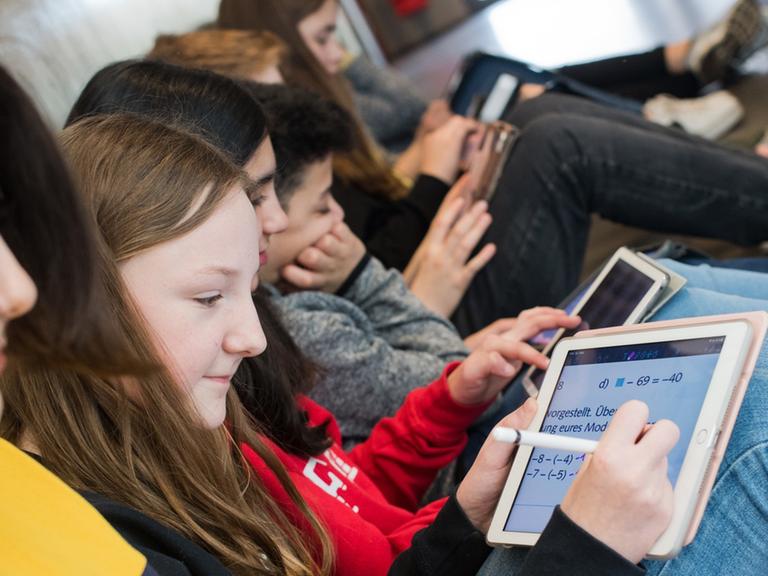 Schüler einer 7. Klasse sitzen auf dem Boden und lernen mit iPads im Matheunterricht an der Oberschule Gehrden in der Region Hannover.