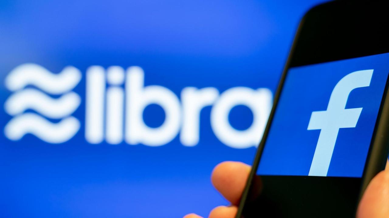 Ein Smartphone mit Facebook-App vor einem Libra-Logo. Ein Smartphone mit Facebook-App vor einem Libra-Logo.