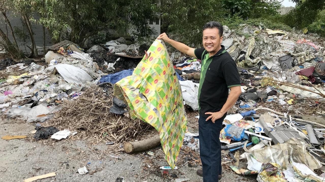 Ein Mann hält Teile eines Plastikmüllbergs in die Kamera. Ein Mann hält Teile eines Plastikmüllbergs in die Kamera.