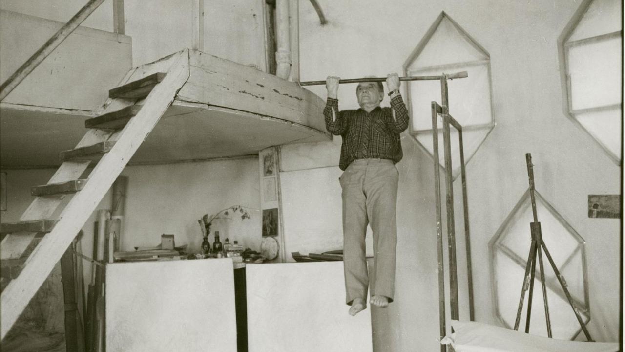 Die Fotografie "Sohn des Architekten Melnikow" von Helga Paris, aus der Serie "Moskau" (1991/92). Ein älterer Mann macht Klimmzüge an einer provisorischen Querverstrebung an einer hölzernen Treppe. Die Fotografie "Sohn des Architekten Melnikow" von Helga Paris, aus der Serie "Moskau" (1991/92). Ein älterer Mann macht Klimmzüge an einer provisorischen Querverstrebung an einer hölzernen Treppe.