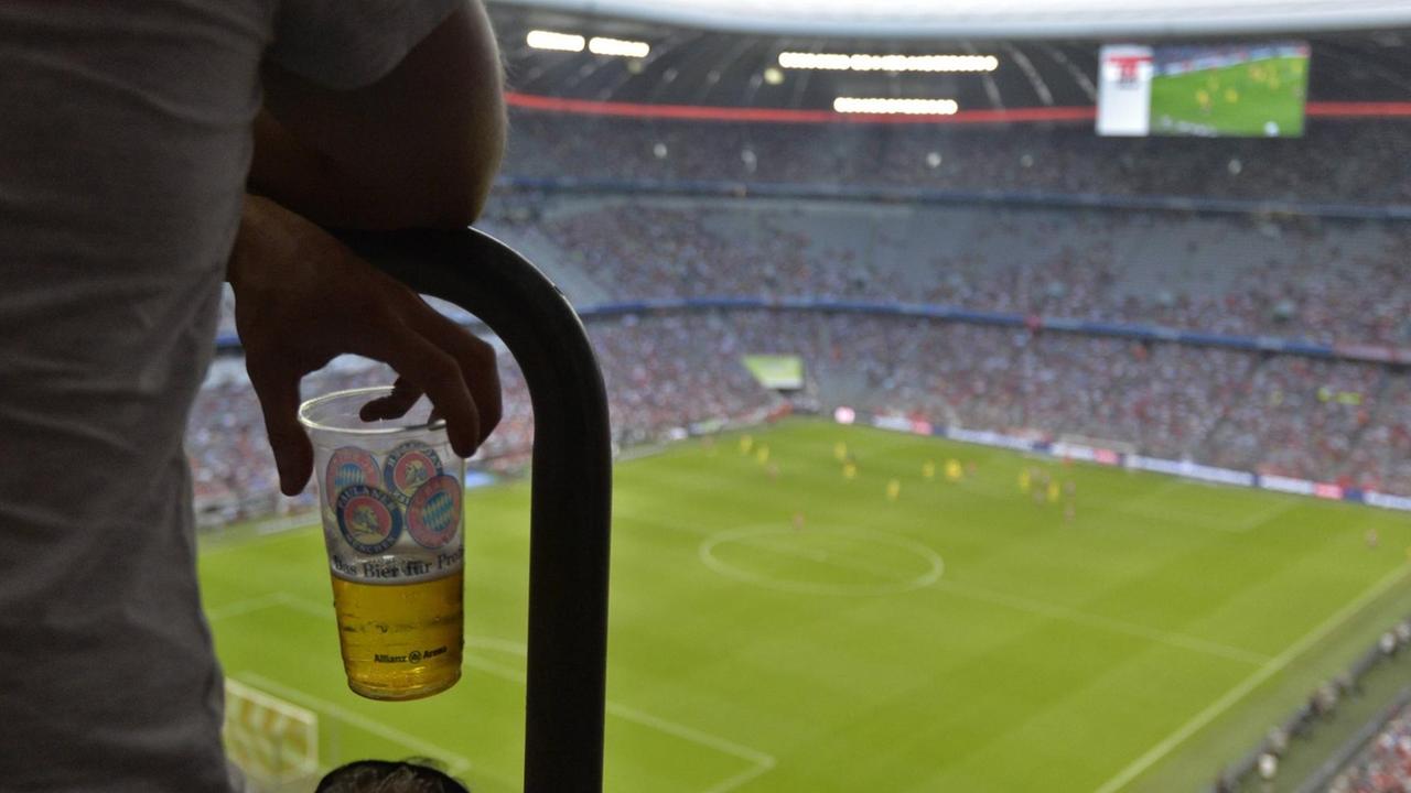 Ein Fan hält einen Plastikbecher mit Bier auf der Tribüne in der Hand. Ein Fan hält einen Plastikbecher mit Bier auf der Tribüne in der Hand.