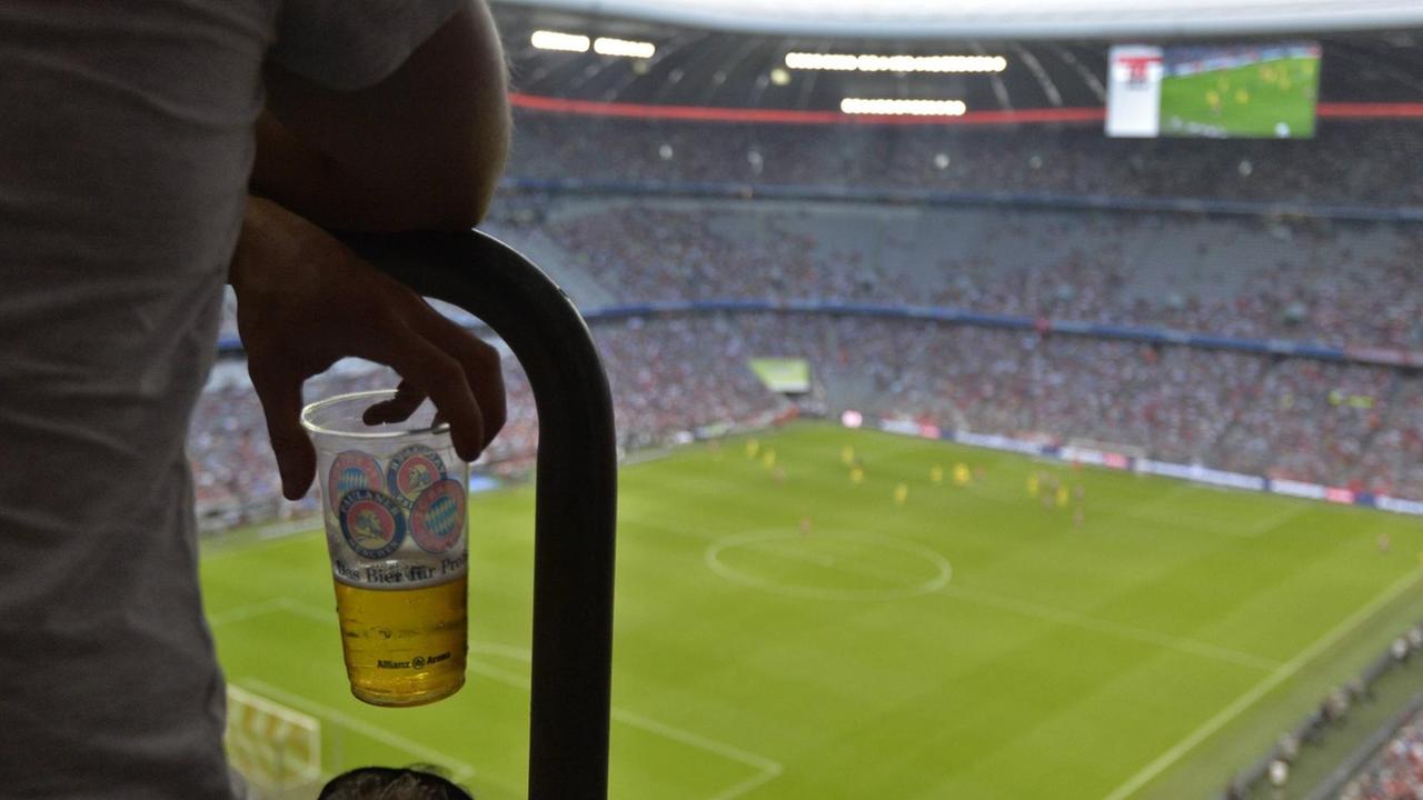 Ein Fan hält einen Plastikbecher mit Bier auf der Tribüne in der Hand.