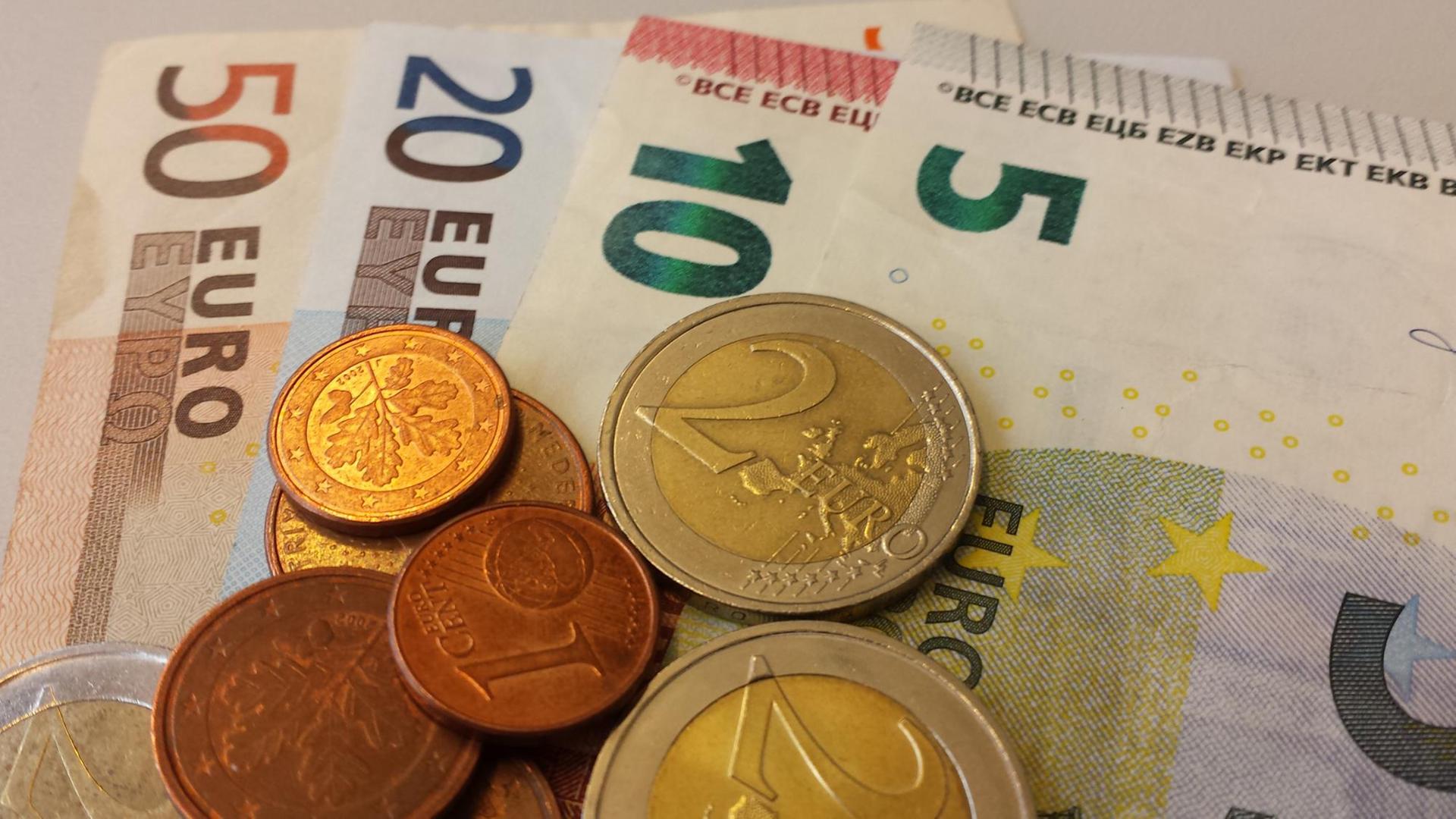 Euro-Geldscheine liegen mit Euro-Münzen auf einem Stapel.