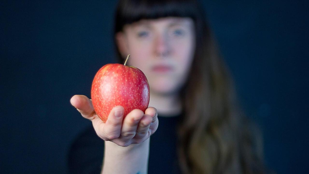 Eine Frau streckt ihre Hand nach vorne aus, in der ein Apfel liegt