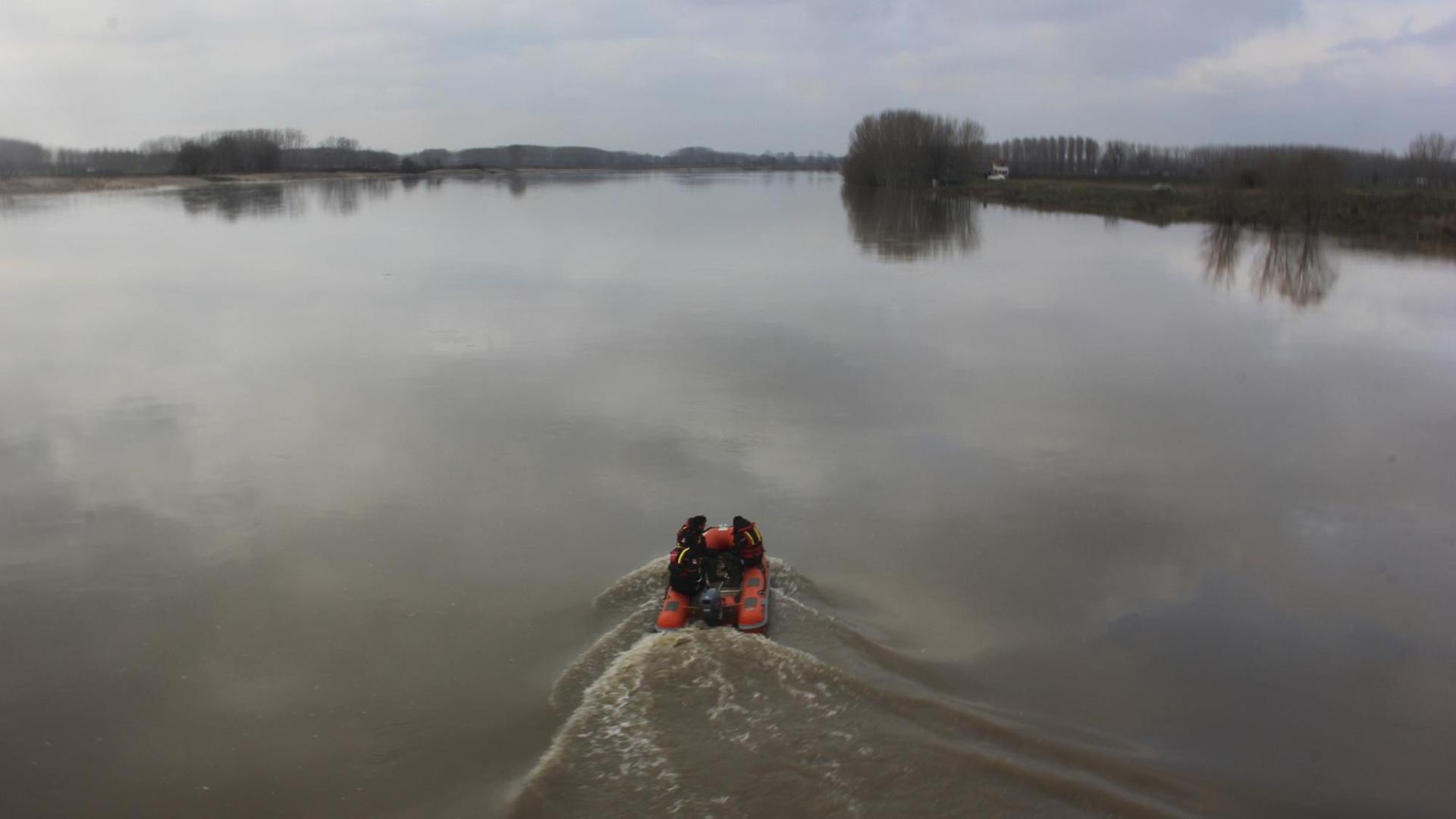 Bild aus der Höhe auf das rote Motor-Schlauchboot, das den graubrauenen Fluss entlangfährt, der von Bäumen gesäumt ist. Bild aus der Höhe auf das rote Motor-Schlauchboot, das den graubrauenen Fluss entlangfährt, der von Bäumen gesäumt ist.