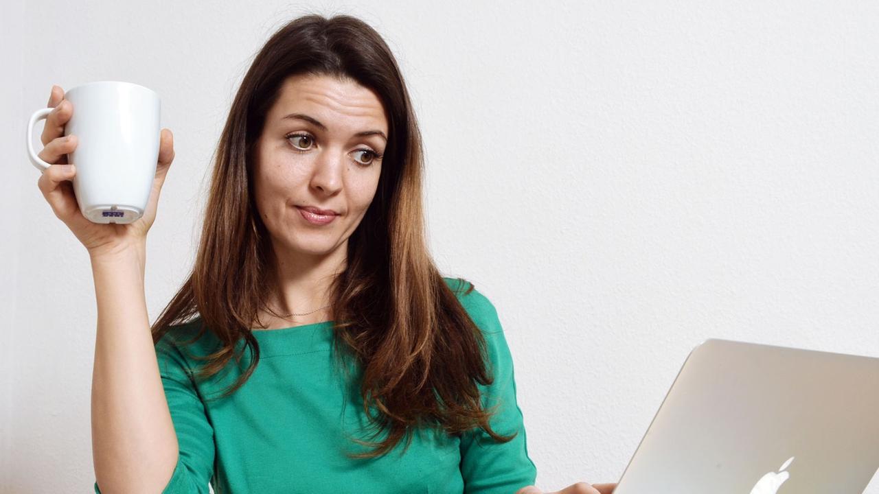 Eine junge Frau sitzt an einem Laptop und schaut skeptisch auf den Bildschirm