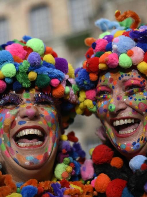 Zwei bunt geschmückte Karnevalistinnen feiern auf dem Düsseldorfer Rathausplatz das Hoppeditz-Erwachen.