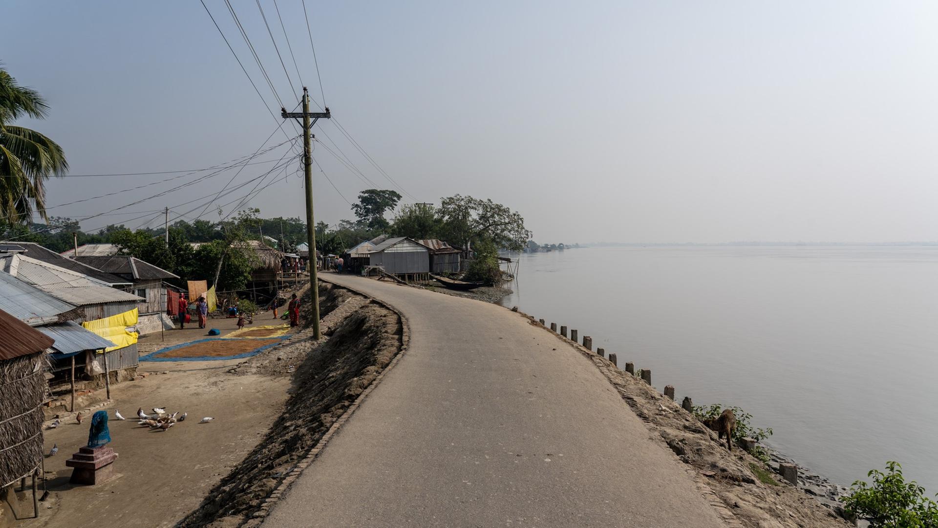 Ein Damm, der gleichzeitig als Straße fungiert - links und im Hintergrund ein Dorf, rechts das Wasser Ein Damm, der gleichzeitig als Straße fungiert - links und im Hintergrund ein Dorf, rechts das Wasser
