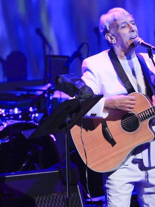 John Cale mit Gitarre auf einer in blaues Licht getauchten Bühne. Neben ihm steht die Sängerin Sky Ferreira.