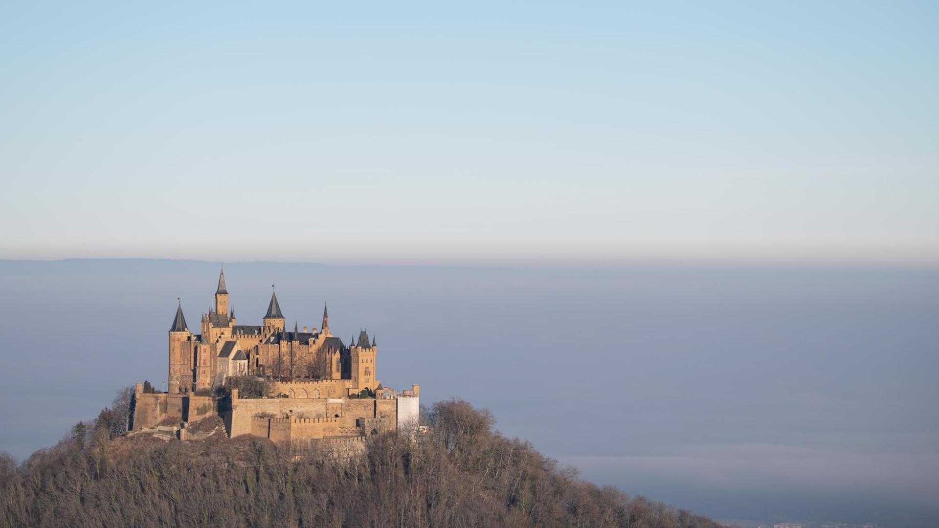 Die Sonne scheint auf die Burg Hohenzollern während das Land dahinter im Nebel liegt.