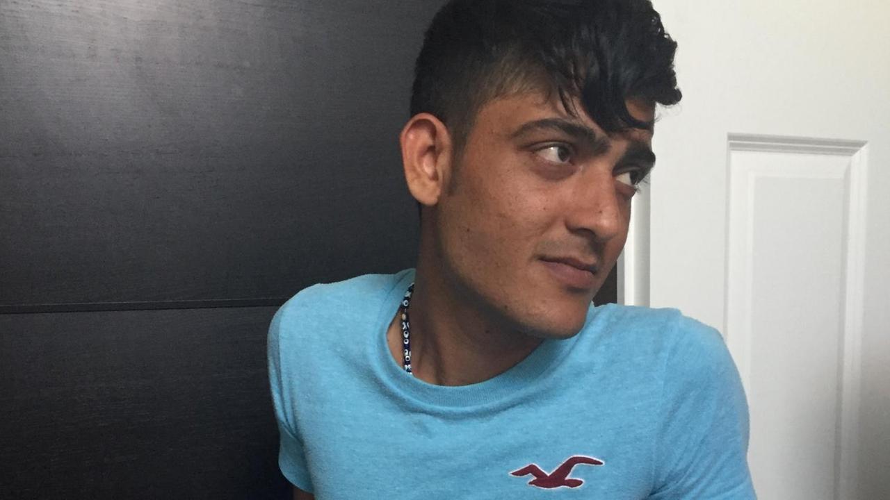 Der afghanische Flüchtling Attaullah Baloz sitzt auf dem Boden, hinter ihm ist eine weiße Holztür und eine schwarze Holzwand zu sehen. Er trägt ein türkisfarbenes T-Shirt. Der afghanische Flüchtling Attaullah Baloz sitzt auf dem Boden, hinter ihm ist eine weiße Holztür und eine schwarze Holzwand zu sehen. Er trägt ein türkisfarbenes T-Shirt.