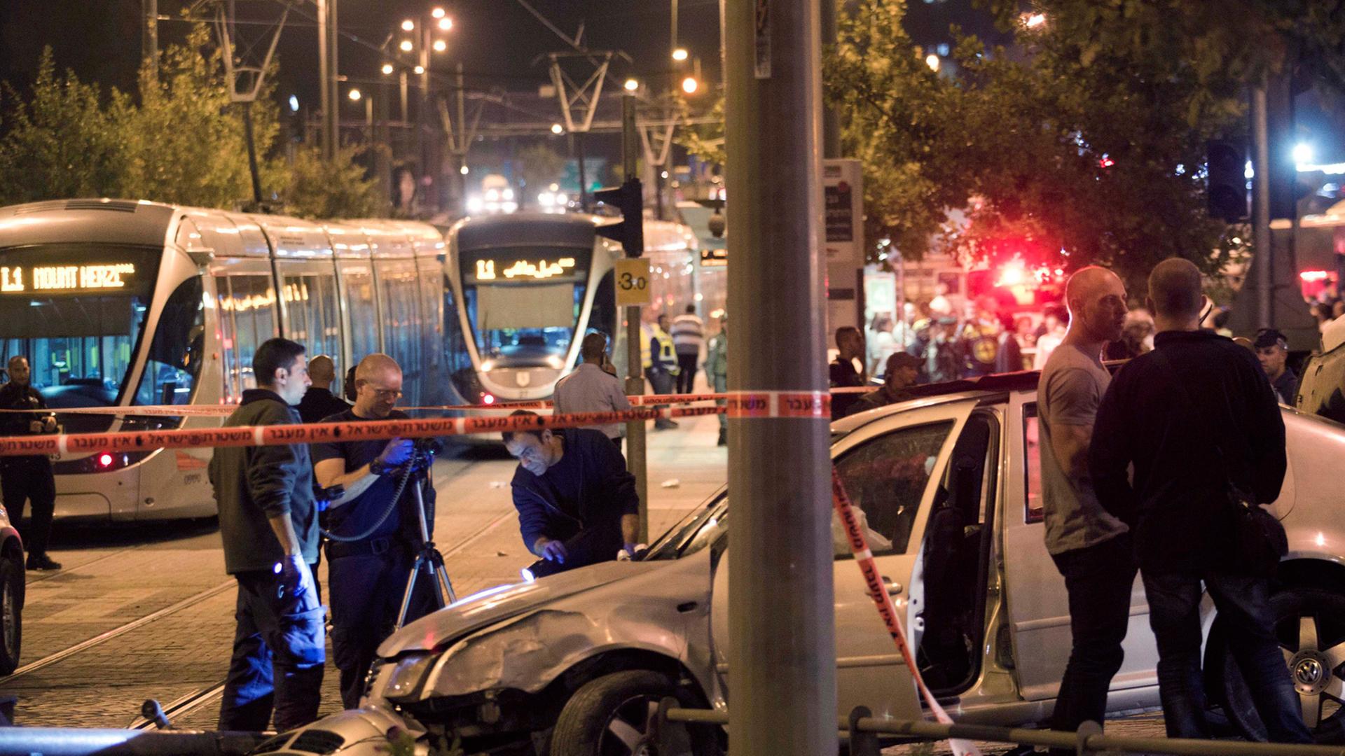 An einer Straßenbahnhaltestelle steht ein verbeultes Auto, umgeben von Absperrband und mehreren Polizisten.
