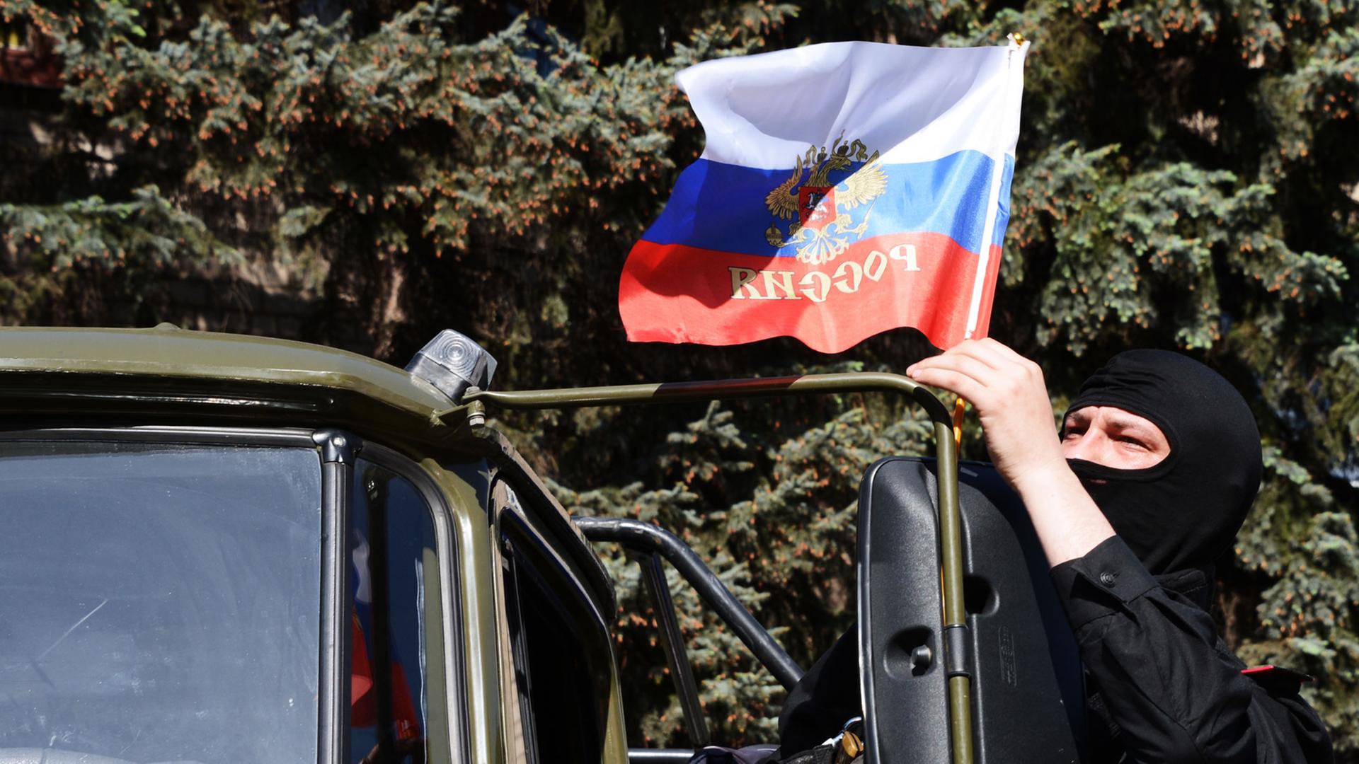 Ein maskierter Mann bringt an einem LKW eine russische Flagge an.