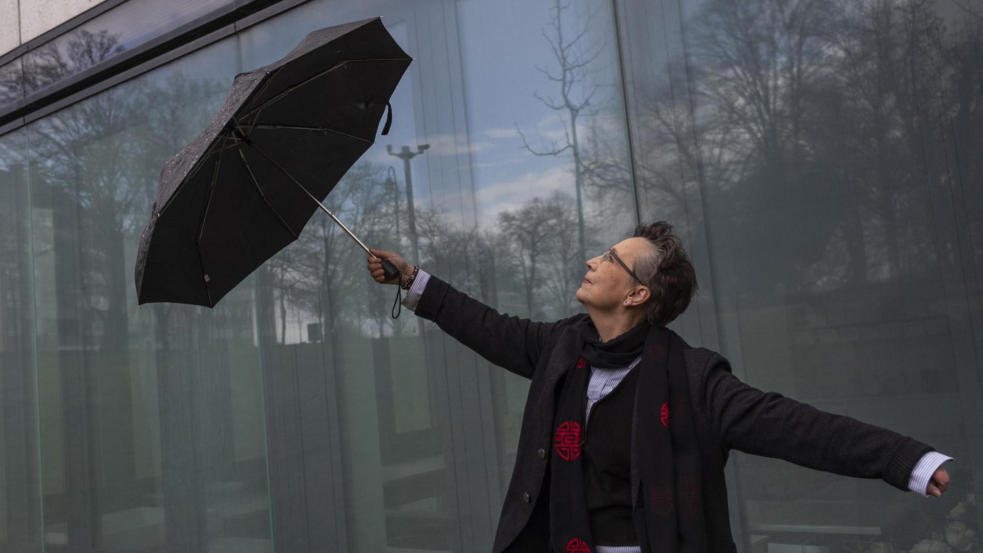Heide-Marie Härtel hat einen Schirm in der Hand und tanzt damit vor einer Glasfassade