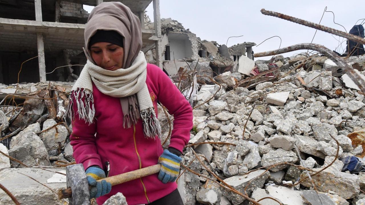 Eine Frau in Aleppo arbeitet mit einem Vorschlaghammer in den Trümmern zerstörter Häuser. 