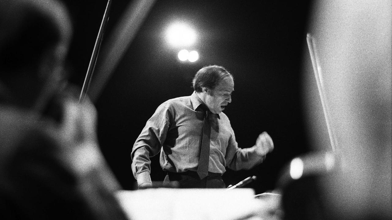 Aus dem Ensemble heraus geschossene Schwarzweißfotografie des Dirgenten Pierre Boulez in dramatischer Anmutung. Aus dem Ensemble heraus geschossene Schwarzweißfotografie des Dirgenten Pierre Boulez in dramatischer Anmutung.
