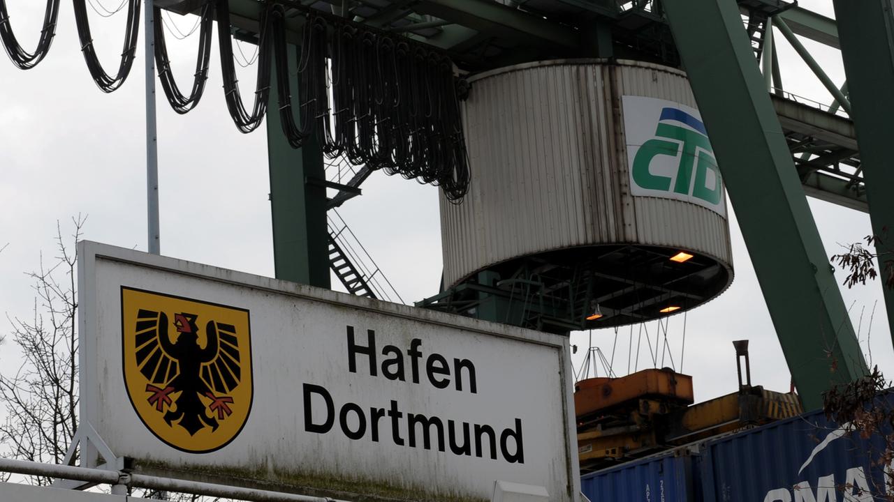 Ein Kran fährt im Container Terminal des Dortmunder Hafens über gestapelte Container.