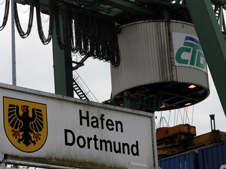 Ein Kran fährt im Container Terminal des Dortmunder Hafens über gestapelte Container.