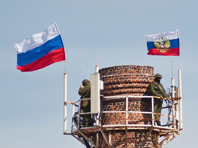 Bewaffnete unter der russischen Fahnen auf einem Schornstein in der Nähe des Marine-Hauptquartiers in Sewastopol
