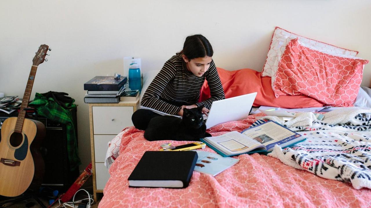 Eine Schülerin sitzt auf ihrem Bett und arbeitet. Homeschooling in Zeiten von Corona. (Symbolbild) Eine Schülerin sitzt auf ihrem Bett und arbeitet. Homeschooling in Zeiten von Corona. (Symbolbild)