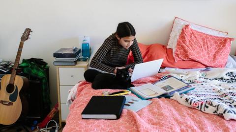 Eine Schülerin sitzt auf ihrem Bett und arbeitet. Homeschooling in Zeiten von Corona. (Symbolbild)