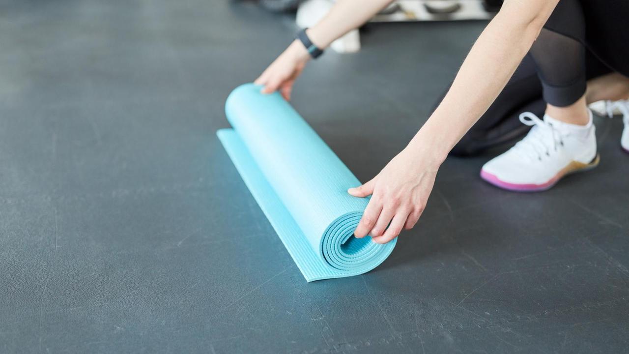 Hände rollen eine Yogamatte aus Hände rollen eine Yogamatte aus