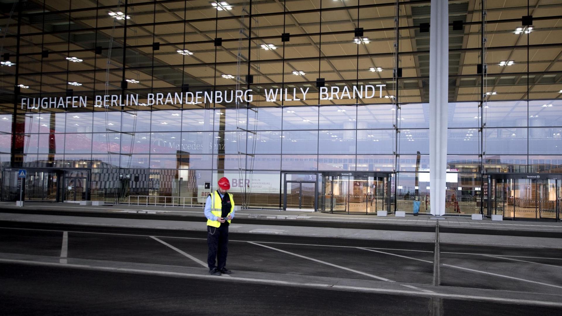 Vor dem Terminal-Gebäude vom neuen und noch nicht fertiggestellten Flughafen BER steht ein einsamer Bauarbeiter.