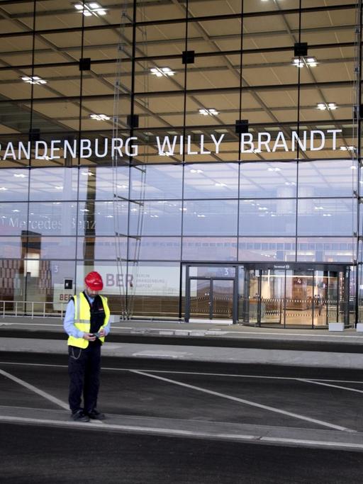 Vor dem Terminal-Gebäude vom neuen und noch nicht fertiggestellten Flughafen BER steht ein einsamer Bauarbeiter.