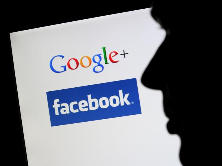 Die Silhouette eines Mannes zeichnet sich vor einem Computerbildschirm mit den Logos von Google+ und Facebook ab.